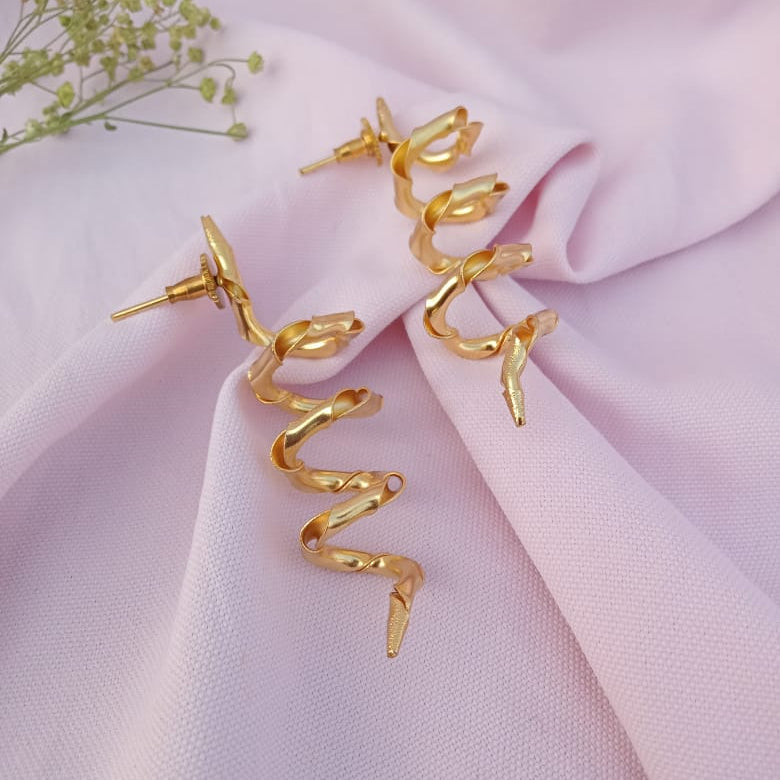 Gold spiral earrings on a pink fabric background